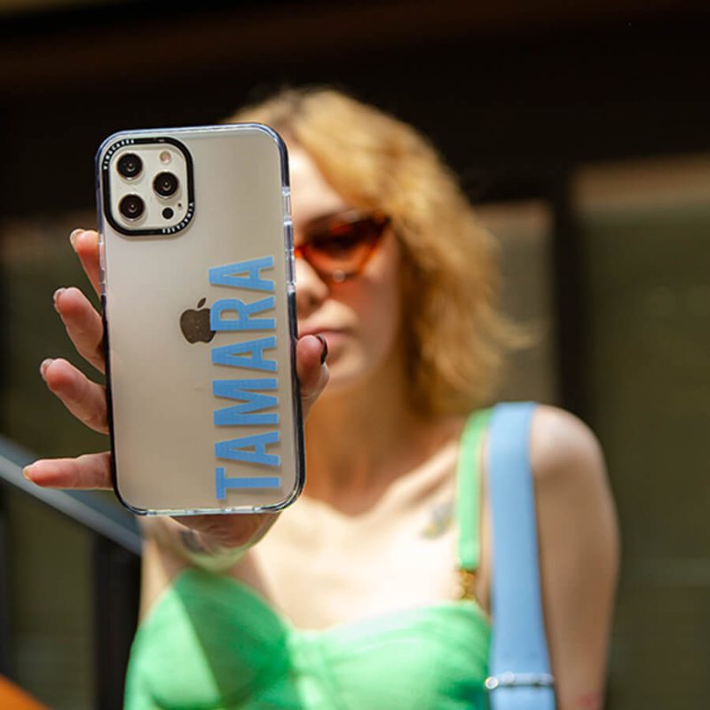 girl with short blonde hair holding and showing an iphone with a case that has the name Tamara printed in blue on it